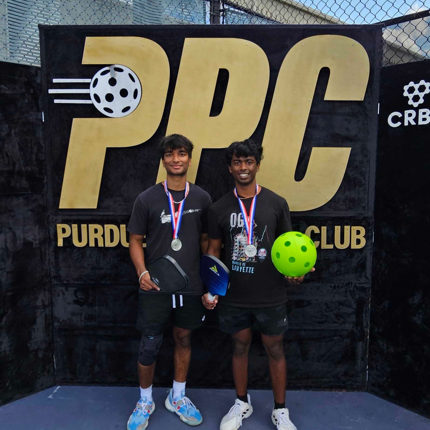 Members with medals in front of the Purdue Pickleball Club sign